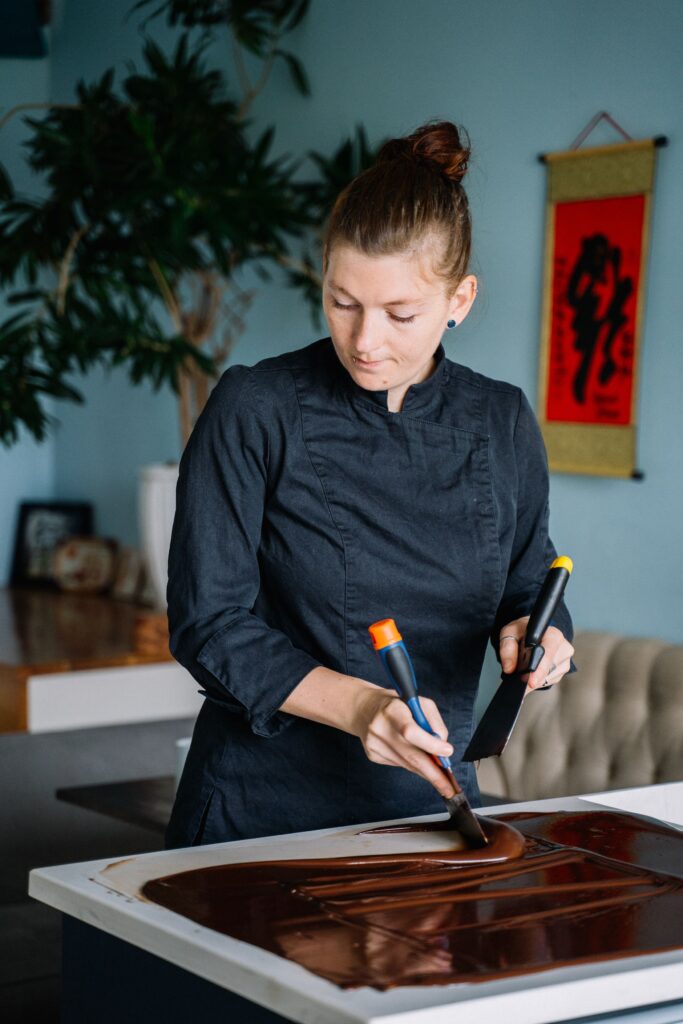 Professional chef in black uniform spreading chocolate syrup indoors.